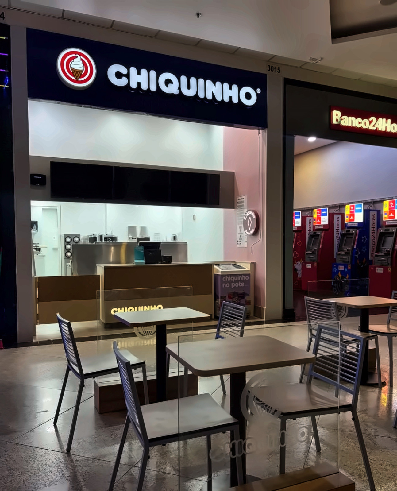 Fachada iluminada da loja Chiquinho Sorvetes em shopping, com mesas em frente